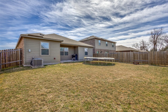 rear view of house featuring a fenced backyard, a trampoline, central AC unit, and a lawn