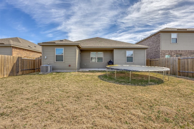 rear view of house with a trampoline, cooling unit, a fenced backyard, and a lawn