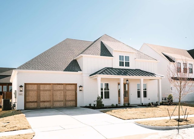 modern farmhouse featuring cooling unit, a garage, a shingled roof, driveway, and a standing seam roof