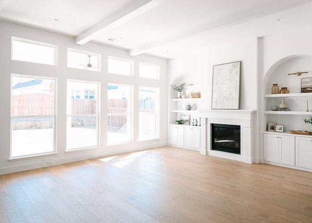 unfurnished living room with recessed lighting, built in features, light wood-style floors, beam ceiling, and a glass covered fireplace