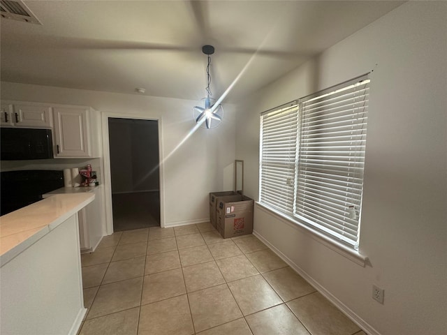 kitchen featuring light tile patterned floors, light countertops, black microwave, white cabinetry, and decorative light fixtures