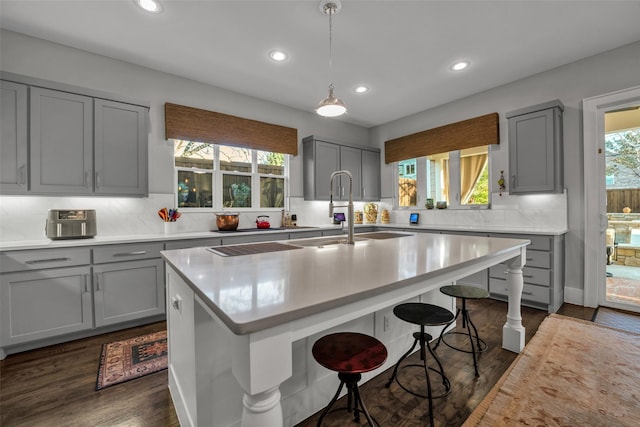 kitchen with a breakfast bar area, gray cabinetry, dark wood-type flooring, a sink, and light countertops