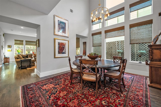 dining room with visible vents, a towering ceiling, an inviting chandelier, wood finished floors, and baseboards