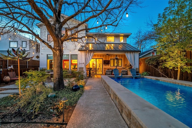 rear view of house featuring ceiling fan, metal roof, fence, a fenced in pool, and a standing seam roof