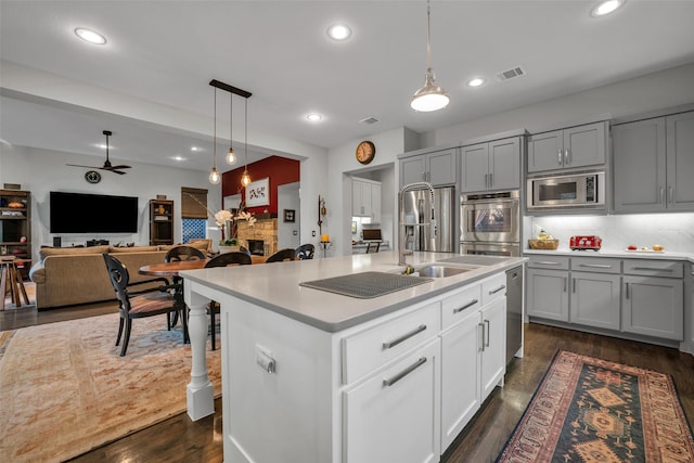 kitchen with a stone fireplace, a sink, light countertops, appliances with stainless steel finishes, and dark wood finished floors