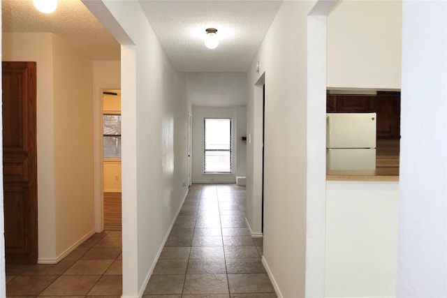 hall featuring a textured ceiling, light tile patterned floors, and baseboards