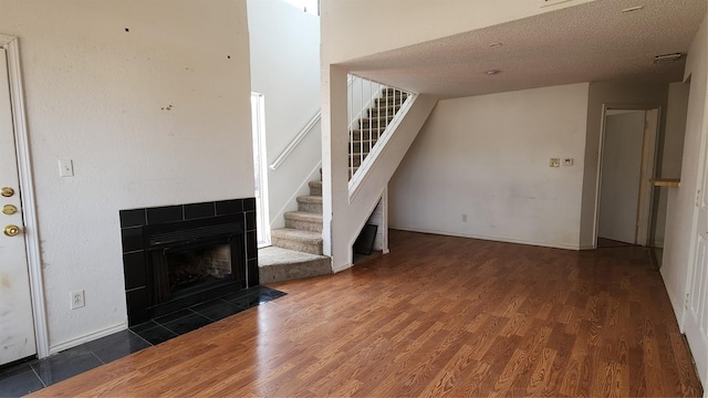 unfurnished living room with a textured ceiling, stairway, wood finished floors, and a tile fireplace