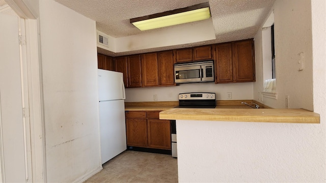 kitchen with a textured ceiling, stainless steel appliances, a peninsula, visible vents, and light countertops