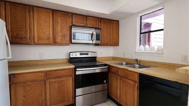 kitchen with appliances with stainless steel finishes, brown cabinetry, light countertops, and a sink