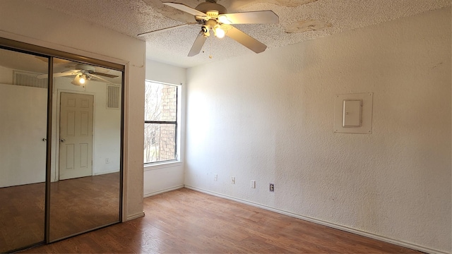 unfurnished bedroom with a textured ceiling, a textured wall, wood finished floors, a closet, and electric panel