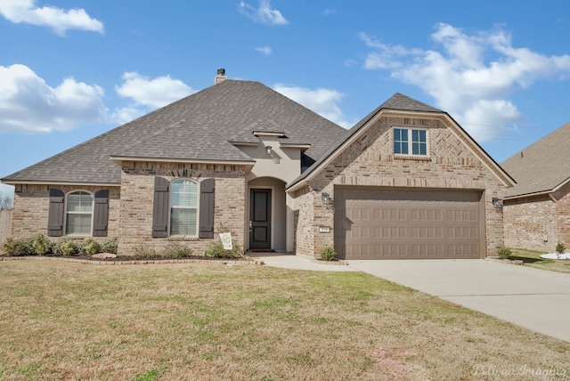 french provincial home with brick siding, a shingled roof, concrete driveway, a front lawn, and a chimney