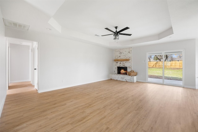 unfurnished living room with visible vents, baseboards, light wood-style floors, a tray ceiling, and a brick fireplace