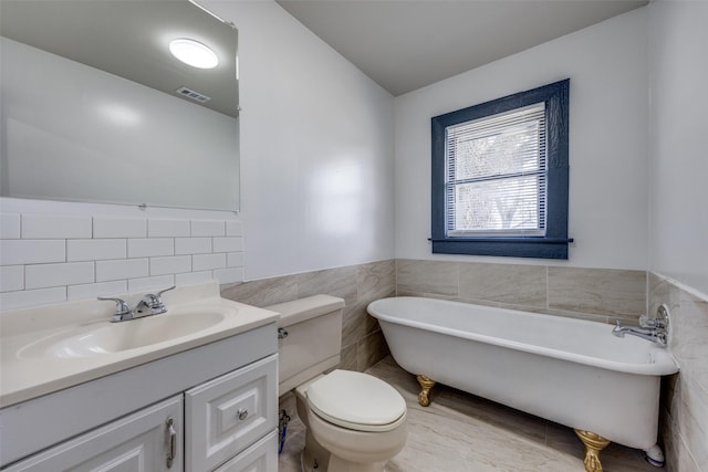 bathroom with visible vents, toilet, a freestanding bath, vanity, and tile walls