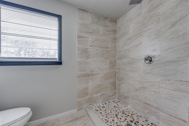 bathroom with baseboards, a tile shower, and toilet