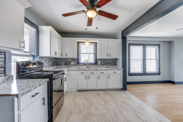 kitchen with black range with electric stovetop, backsplash, white cabinets, a sink, and baseboards