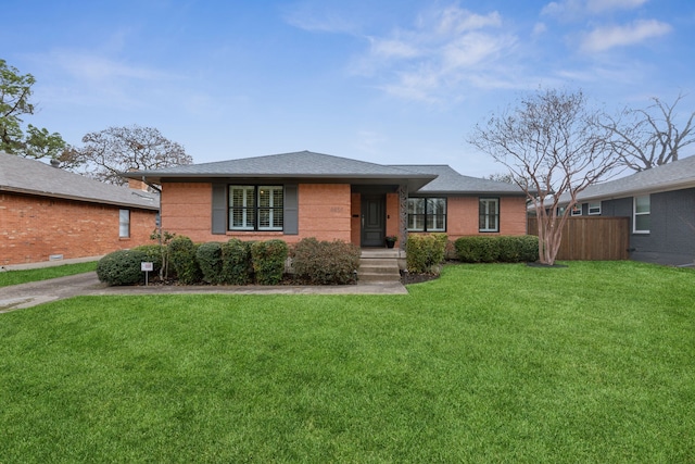 view of front of property featuring brick siding, fence, a front lawn, and roof with shingles