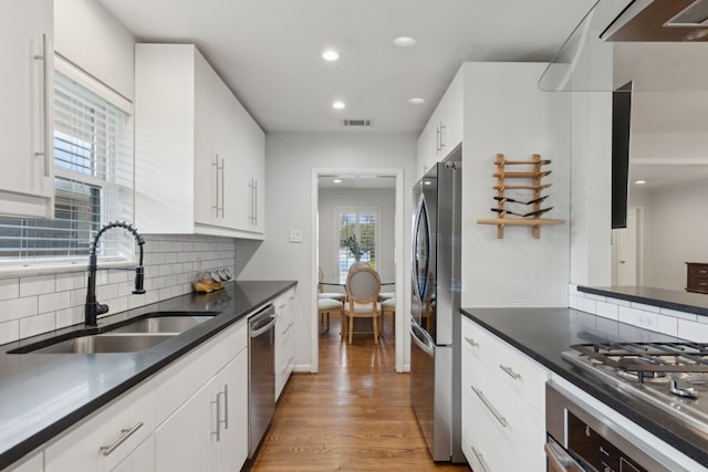 kitchen with decorative backsplash, dark countertops, appliances with stainless steel finishes, light wood-style floors, and a sink