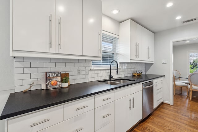 kitchen with a sink, visible vents, light wood-type flooring, dishwasher, and dark countertops