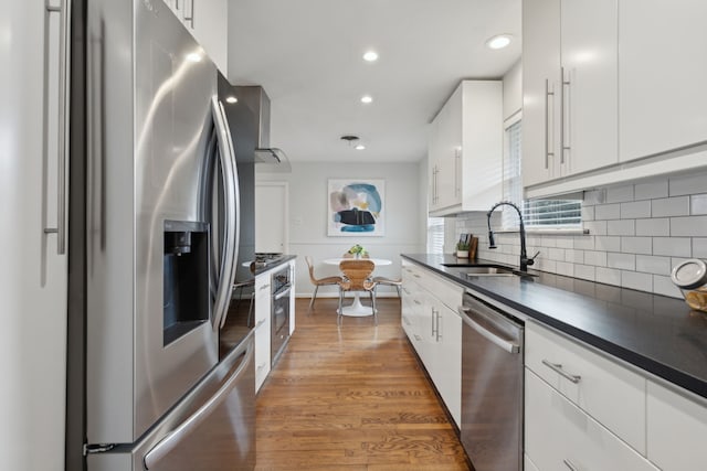 kitchen featuring tasteful backsplash, white cabinets, dark countertops, appliances with stainless steel finishes, and a sink