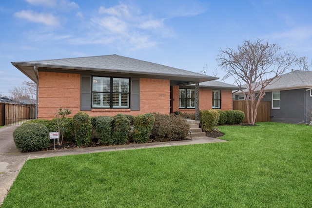 view of front facade featuring brick siding, fence, a front lawn, and roof with shingles