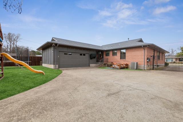 view of front of house with a playground, central air condition unit, a front yard, fence, and a garage