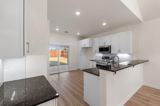 kitchen with backsplash, light wood-style flooring, appliances with stainless steel finishes, white cabinetry, and dark stone countertops