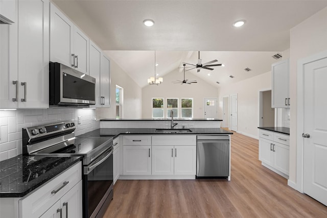 kitchen with dark countertops, lofted ceiling, a peninsula, stainless steel appliances, and a sink