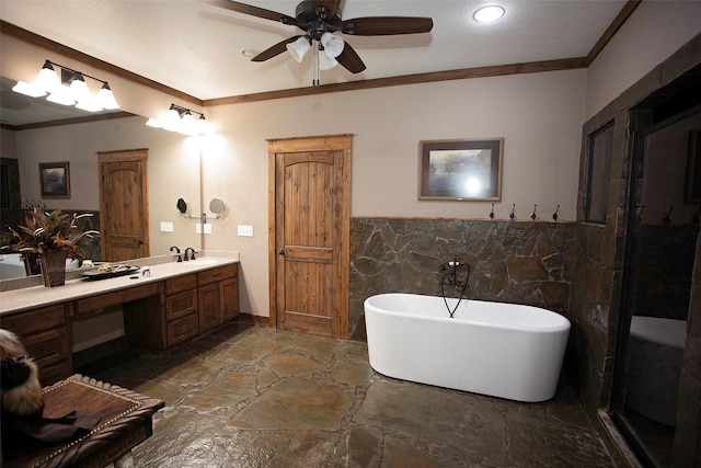 bathroom featuring crown molding, tile walls, a freestanding bath, stone finish flooring, and vanity