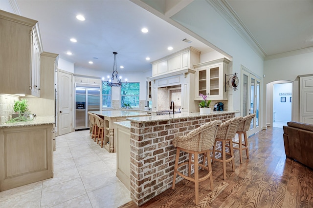 kitchen with arched walkways, crown molding, a breakfast bar area, glass insert cabinets, and built in refrigerator