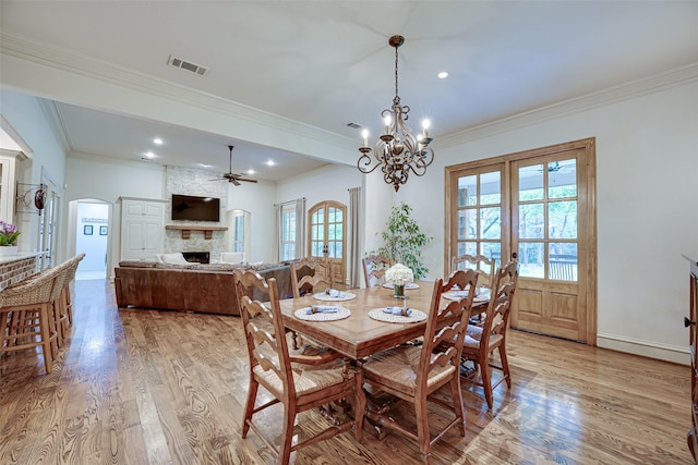 dining area featuring arched walkways, a fireplace, visible vents, ornamental molding, and light wood-type flooring