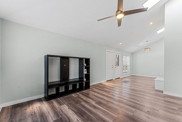 unfurnished living room featuring ceiling fan, vaulted ceiling with skylight, wood finished floors, and baseboards