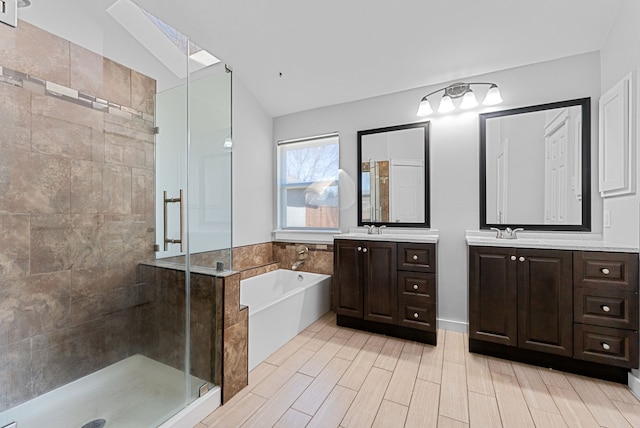 bathroom with two vanities, a stall shower, a garden tub, and vaulted ceiling with skylight