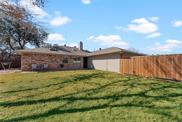 back of property with a fenced backyard, brick siding, a yard, a chimney, and a patio area