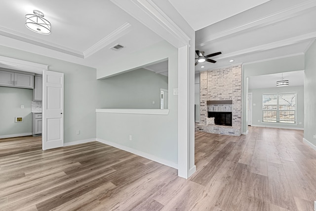 unfurnished living room featuring crown molding, visible vents, a ceiling fan, a brick fireplace, and light wood-type flooring