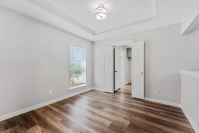 empty room with a tray ceiling, baseboards, and wood finished floors