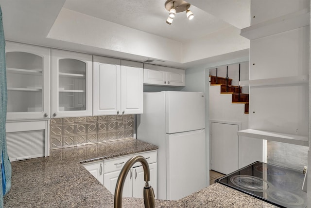 kitchen with glass insert cabinets, white cabinetry, dark stone counters, and freestanding refrigerator