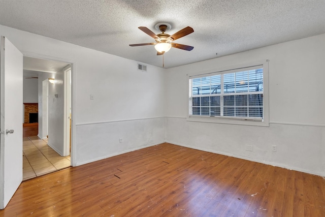 spare room with ceiling fan, a textured ceiling, visible vents, and wood finished floors