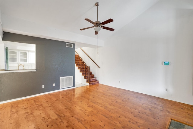 unfurnished living room with a ceiling fan, stairs, visible vents, and wood finished floors