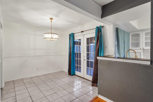 unfurnished dining area featuring tile patterned floors, baseboards, a chandelier, and french doors