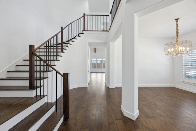 stairway with a notable chandelier, a towering ceiling, baseboards, and hardwood / wood-style flooring