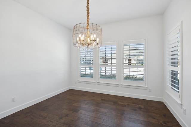 unfurnished dining area with dark wood-style flooring, an inviting chandelier, and baseboards