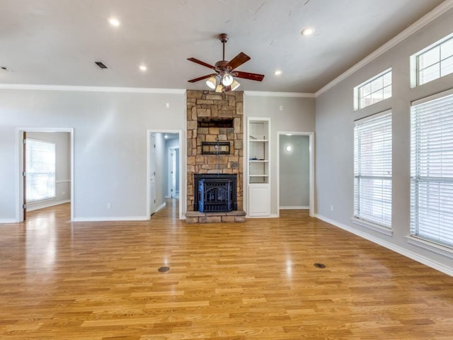 unfurnished living room featuring a wealth of natural light, a stone fireplace, visible vents, and crown molding