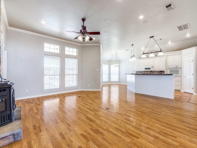 unfurnished living room featuring light wood finished floors, visible vents, a wood stove, crown molding, and ceiling fan with notable chandelier