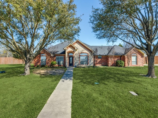 ranch-style home featuring roof with shingles, a front yard, and brick siding