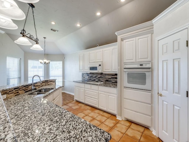 kitchen featuring lofted ceiling, backsplash, white cabinets, a sink, and white appliances