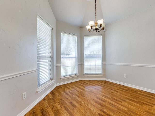 unfurnished dining area with lofted ceiling, baseboards, a chandelier, and wood finished floors