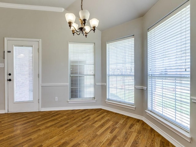 unfurnished dining area featuring vaulted ceiling, baseboards, wood finished floors, and an inviting chandelier