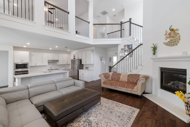 living room with dark wood finished floors, recessed lighting, visible vents, stairway, and a glass covered fireplace