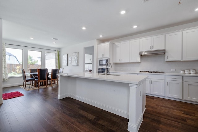 kitchen with dark wood-type flooring, built in microwave, light countertops, under cabinet range hood, and a sink