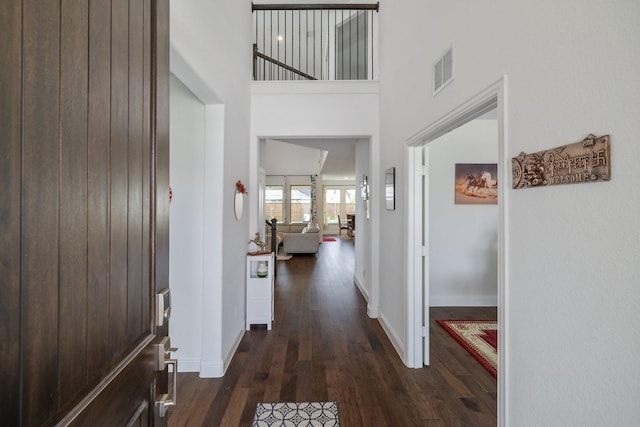 corridor with dark wood-style floors, a towering ceiling, visible vents, and baseboards